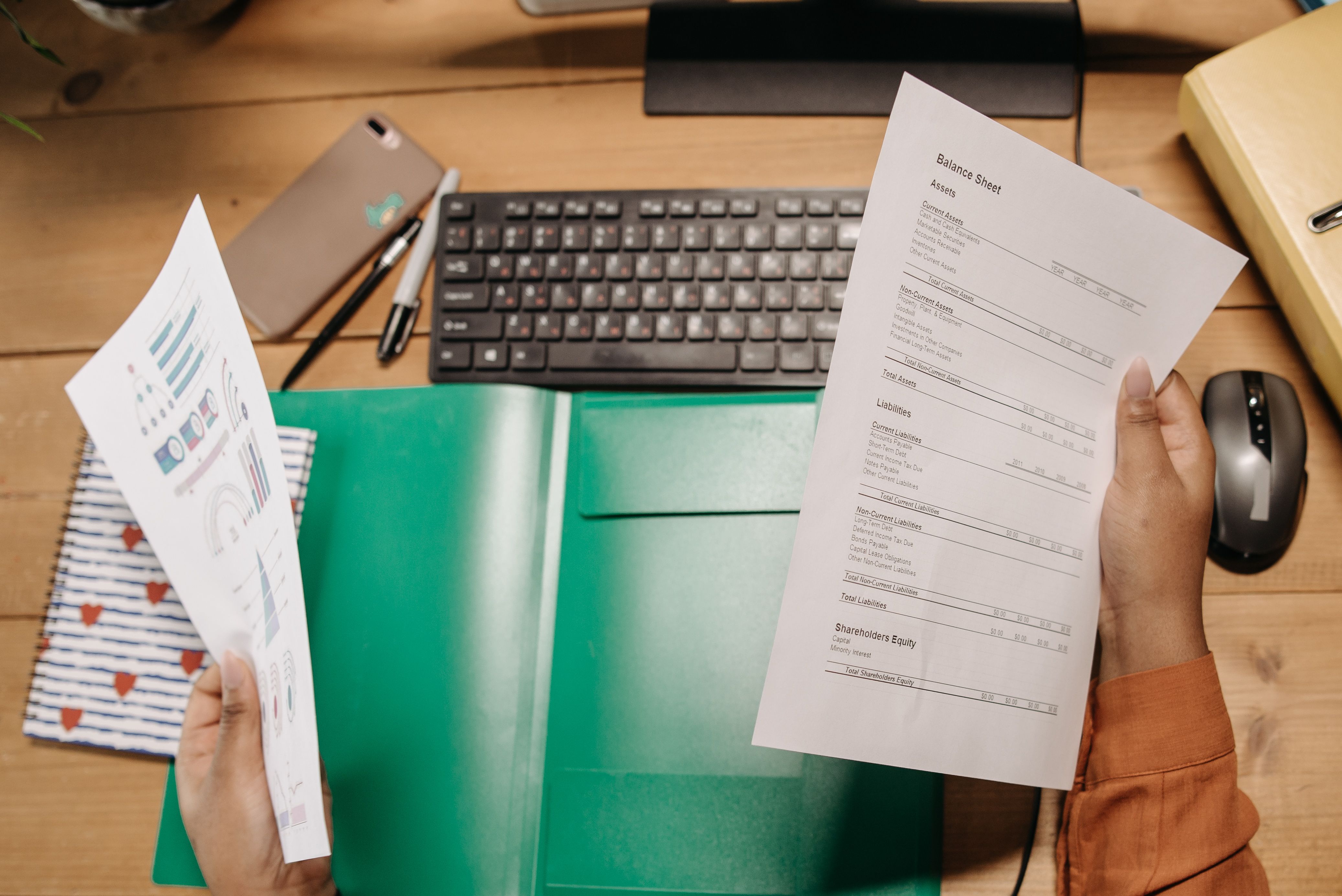 Hands holding and reviewing balance sheets over a desk with a keyboard and stationery