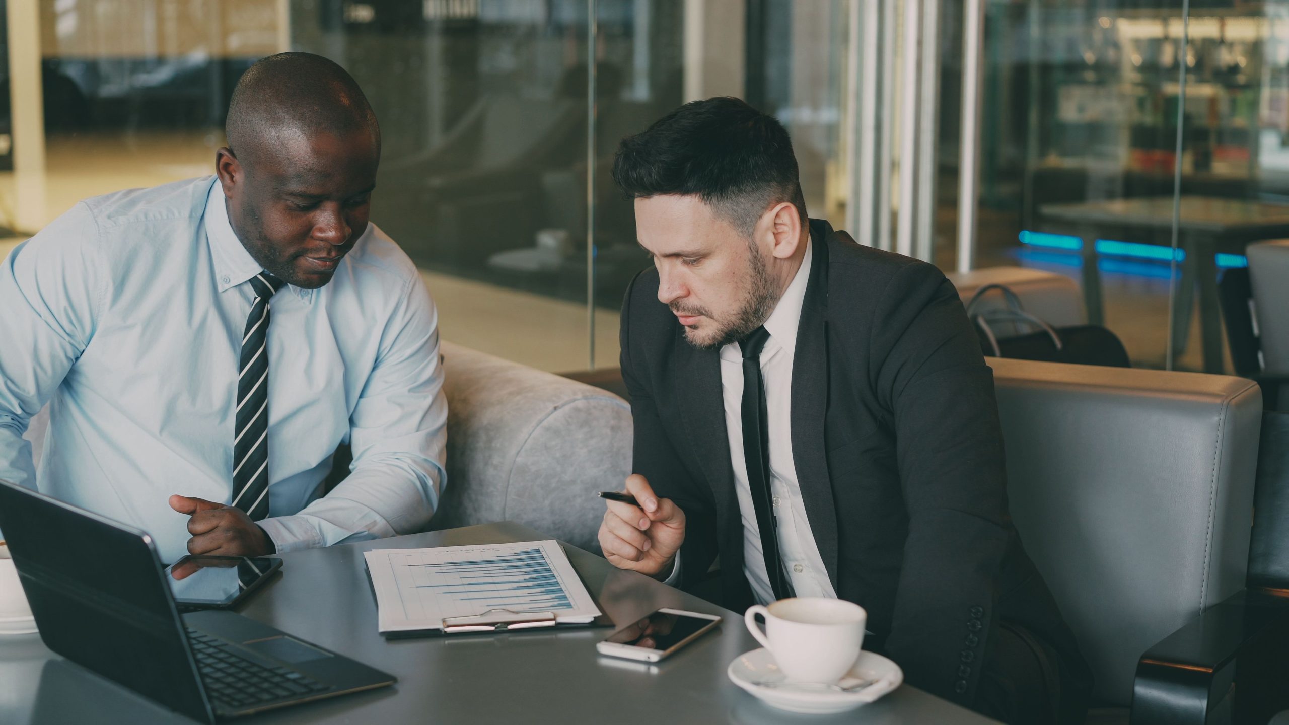 Two business professionals reviewing a financial report with a laptop and coffee in an office